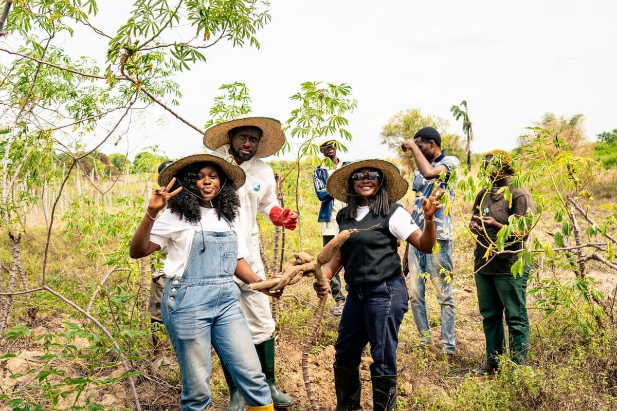 A group of young farmers in a field holding harvested cassava roots, smiling